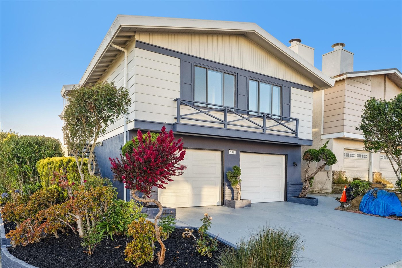 Renovated home exterior with fresh two-tone paint, new garage doors, and landscaping